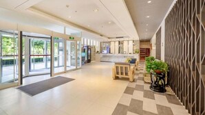 Eine Hotelhalle mit Empfangsschalter, Check-in-Bereich und einer Sitzecke mit einer Bank und Topfpflanzen.