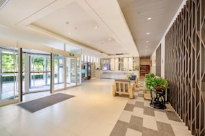 Et hotellobby med reception, indtjekningsskranke og et loungeområde med bænk og potteplanter.