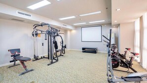 Ein Fitnessraum mit Trainingsgeräten, einer Projektionsleinwand und einem gemusterten Teppich.