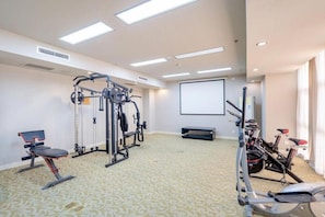 Et fitnessrum med træningsudstyr, en projektorskærm og et mønstret tæppe.