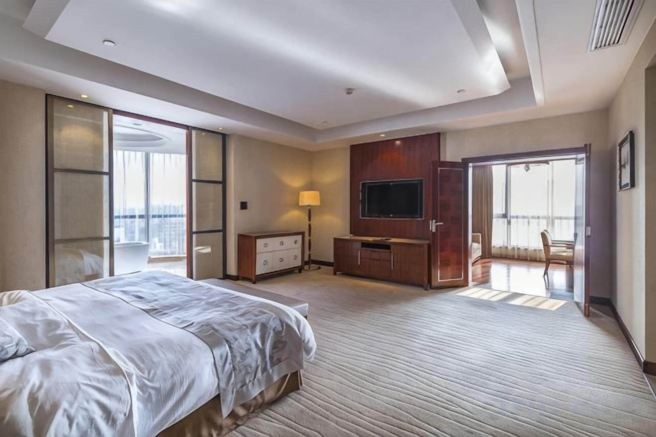 Habitación de hotel con una cama grande, televisión, escritorio y balcón.