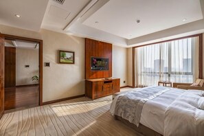 A hotel room with a large bed, a television, a wooden cabinet, and a view of the city through large windows. - Dongdu Narada Grand Hotel (Yixing)