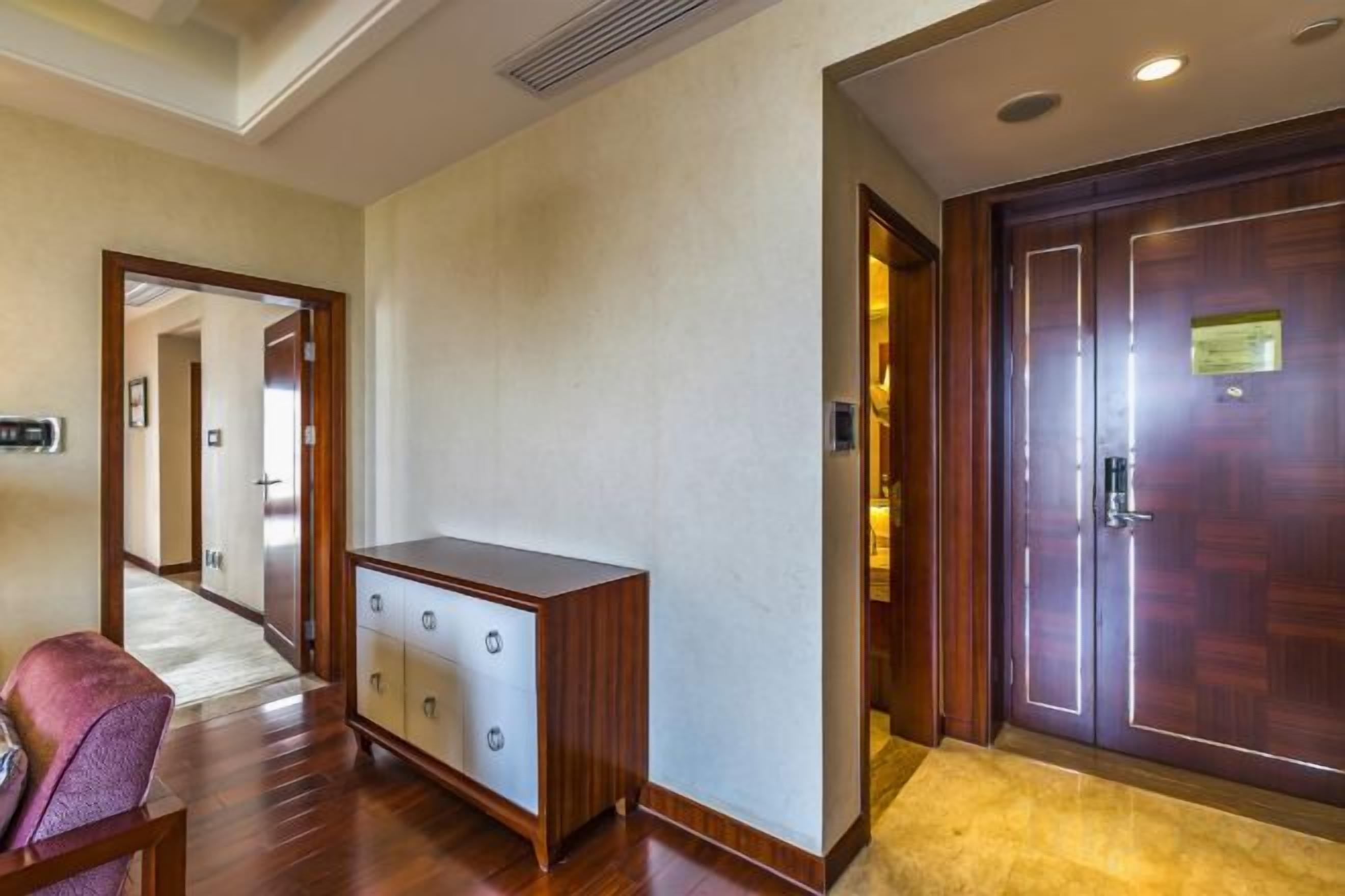 Un couloir d’hôtel avec une armoire en bois, une porte avec une plaque et une entrée recouverte de moquette.