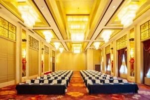 Un salón de conferencias con filas de mesas y sillas, suelo alfombrado y decoración tradicional.