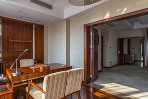 A room with a wooden desk, a chair, a lamp, and a large open doorway leading to another room.