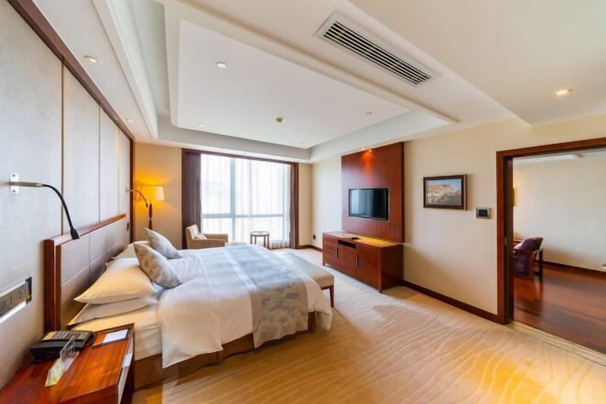 A hotel room with a bed, bedside table, TV, and a large window.