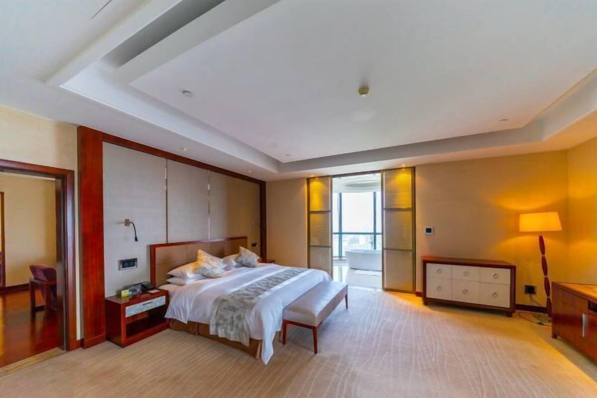 A hotel room with a large bed, a bedside table, a chair, a desk, and a window with a view.