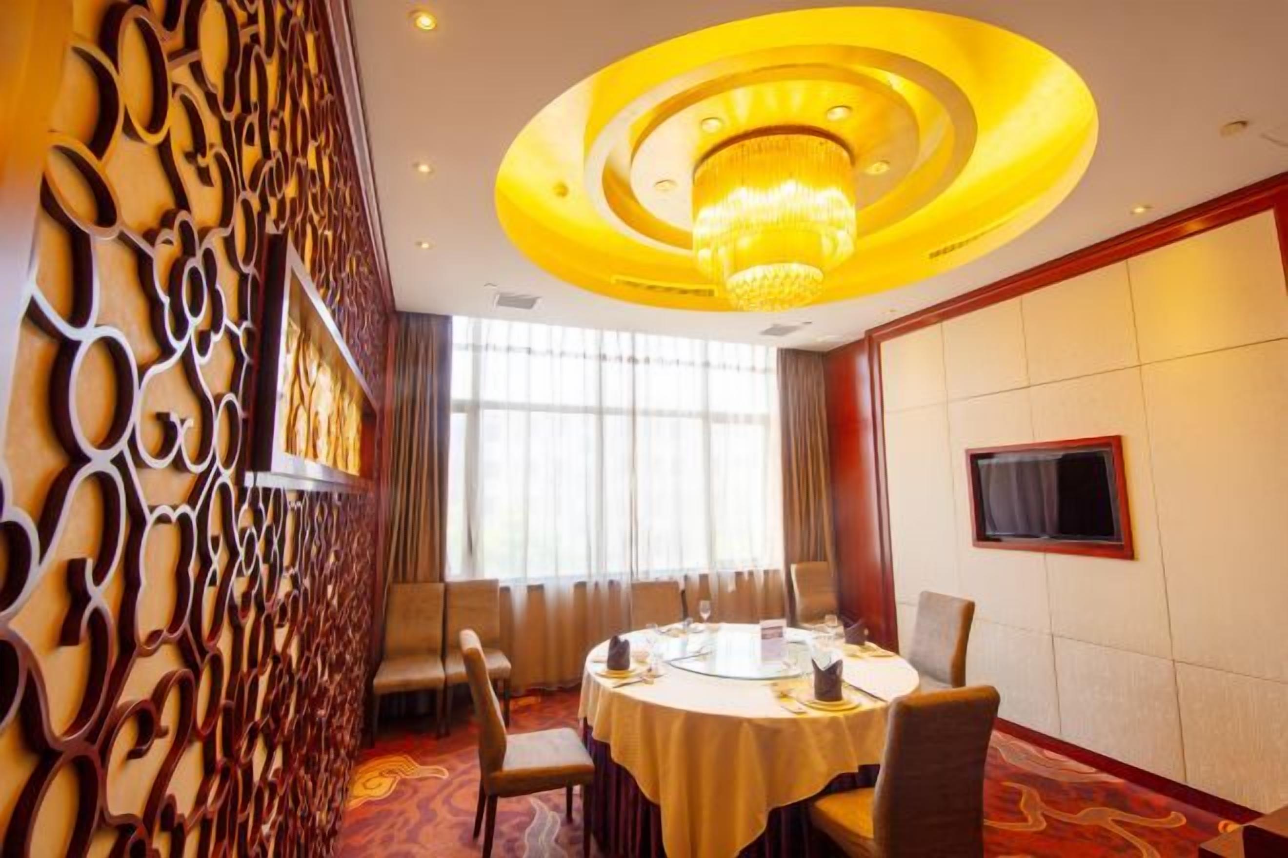 A conference room with a round table, chairs, a chandelier, a television, and a decorative wall panel.