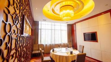 A conference room with a round table, chairs, a chandelier, a television, and a decorative wall panel.