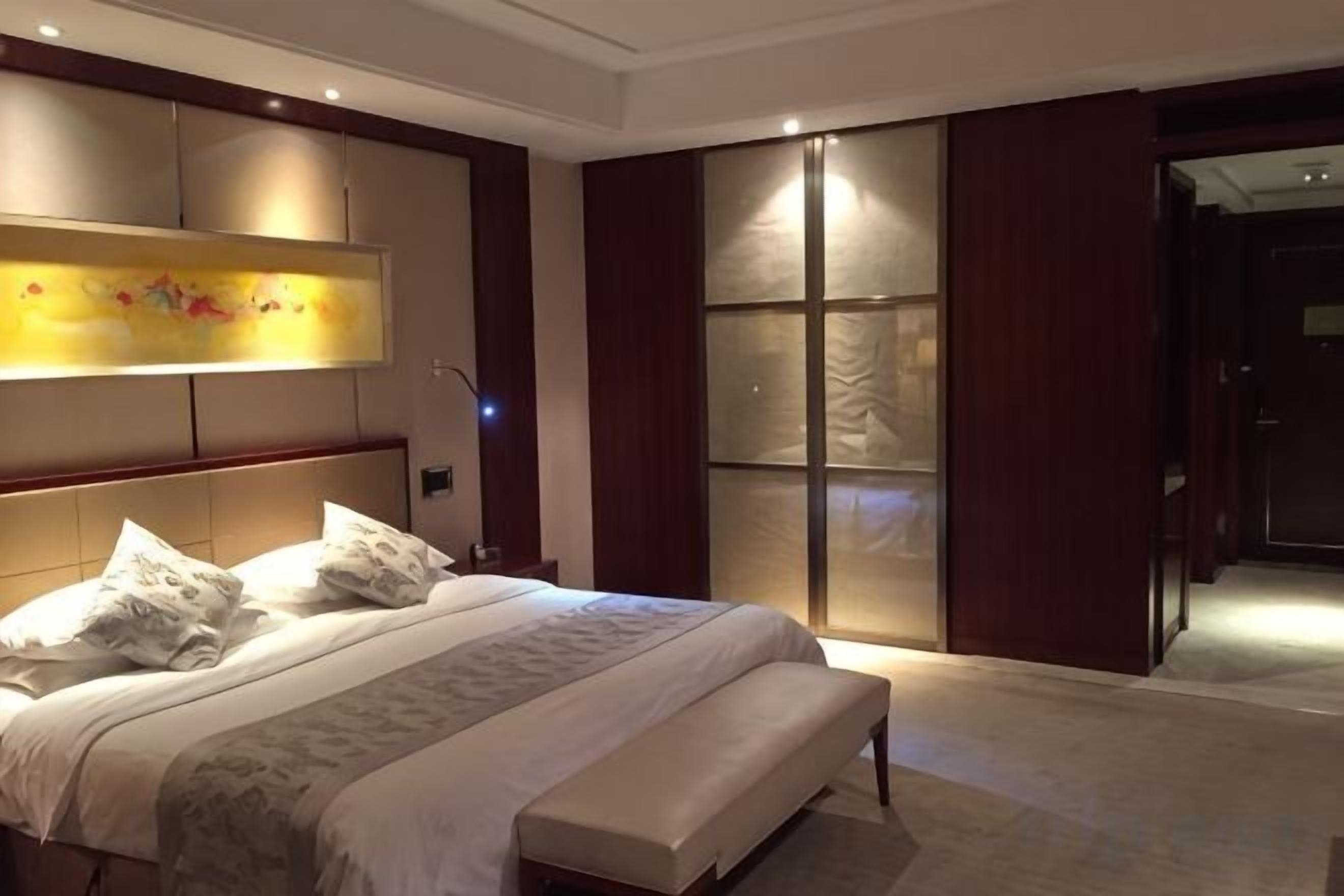 Habitación de hotel con una cama grande, una mesita de noche, un televisor montado en la pared y un armario con puertas correderas.