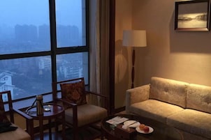Habitación de hotel con un ventanal grande, un sofá, una silla, una mesita y una lámpara.
