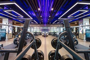 Un gimnasio con equipamiento de levantamiento de pesas, paredes con espejos y un diseño moderno en el techo.