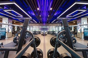 Un gimnasio con equipamiento de levantamiento de pesas, paredes con espejos y un diseño moderno en el techo.