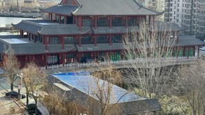 A traditional multi-story building with a red facade and grey roof, surrounded by modern high-rise buildings and a body of water. - Greentree Inn Shandong Linyi Yishui County Angel G (Linyi)