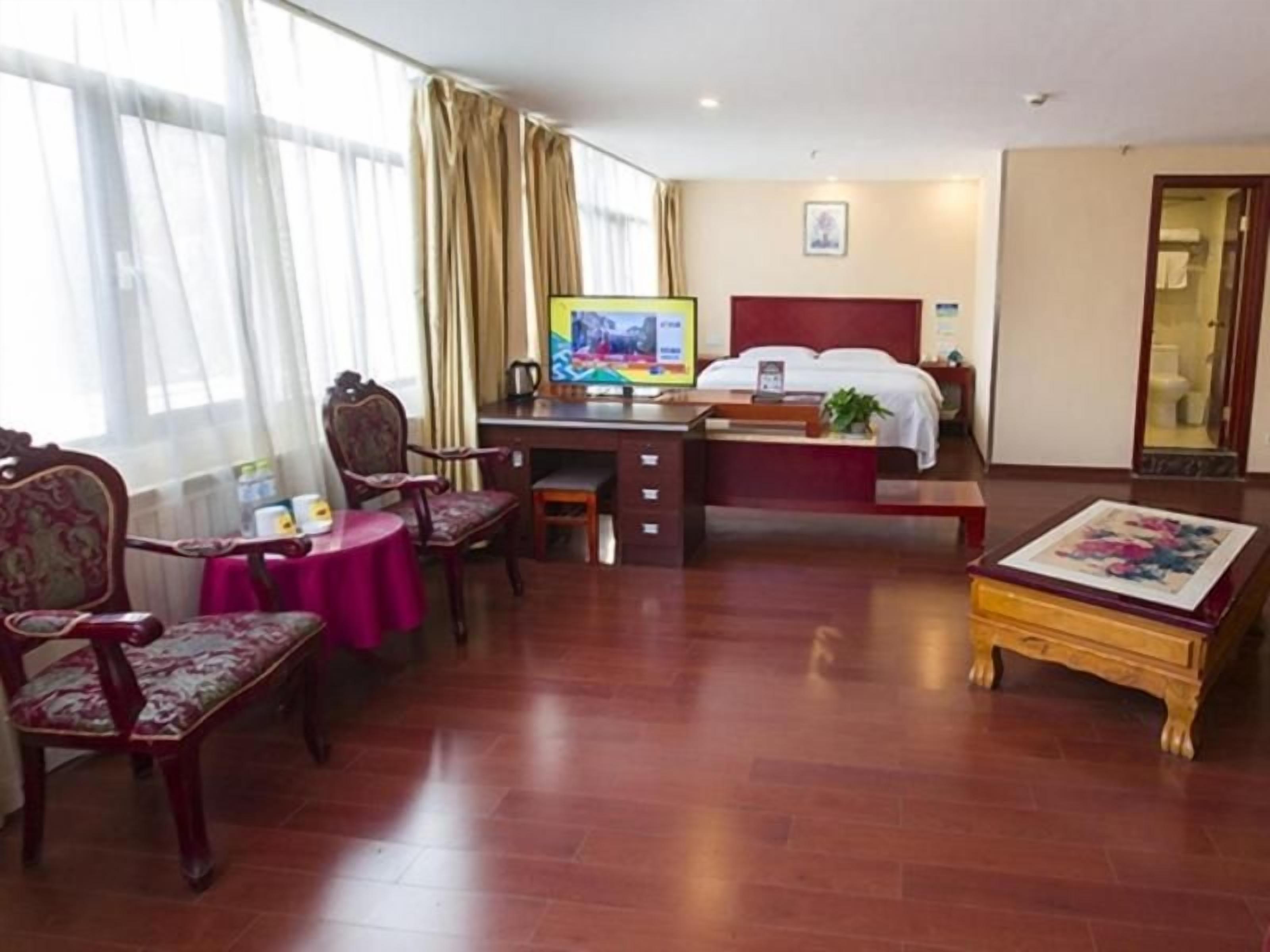 A hotel room with a bed, desk, chairs, a television, and a painting.