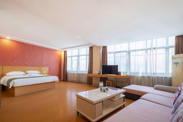 Une chambre d’hôtel avec un lit, un bureau avec une télévision, un canapé et de grandes fenêtres.