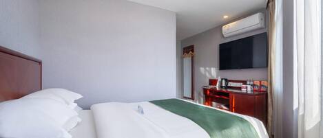 Una habitación de hotel con cama, escritorio, televisor y aire acondicionado.
