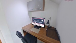 A small office space with a desk, a chair, a computer, a lamp, and a sign advertising Covstays serviced apartments in Coventry Central. - Victoria House - Deluxe Studio by CovStays (Coventry)