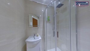 A modern bathroom with a glass shower enclosure, a white sink, and a mirror above it. - Victoria House - Deluxe Studio by CovStays (Coventry)