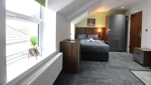 A bedroom with a bed, a dresser, a radiator, a window with a plant, and a painting on the wall. - Victoria House - Deluxe Studio by CovStays (Coventry)