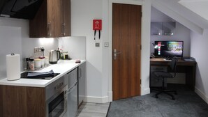 A compact kitchen with a stove, oven, and a coffee maker. There is a wooden door leading to a bedroom with a desk and a computer monitor. - Victoria House - Deluxe Studio by CovStays (Coventry)