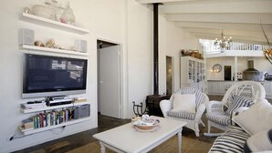 Een woonkamer met een flatscreen televisie, boekenkasten, een salontafel en witte rieten meubels.