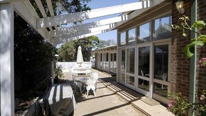 Een overdekt terras met een pergola, een witte hek en een bakstenen gebouw met grote ramen.