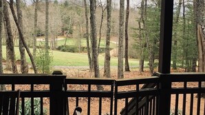 A view from a wooden deck overlooking a golf course with trees in the background.