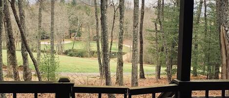 Blick von einer Holzterrasse auf einen Golfplatz, im Hintergrund Bäume.