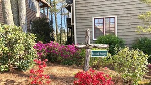 A wooden signpost with a green sign reading "Second Heaven" in front of a house with a window and a balcony.