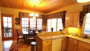 A kitchen with wooden cabinets, a dishwasher, a dining table with chairs, and a window with curtains.