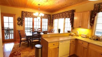 A kitchen with wooden cabinets, a dishwasher, a dining table with chairs, and a window with curtains.