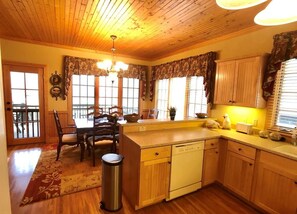 A kitchen with wooden cabinets, a dishwasher, a dining table with chairs, and a window with curtains. - Mountain walk-in level condo! (Cashiers)
