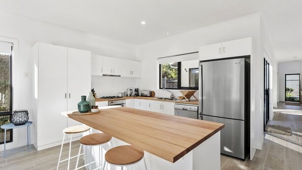 Een moderne keuken met witte kastjes, een houten eiland met krukken, roestvrijstalen apparatuur en een groot raam dat natuurlijk licht binnenlaat.