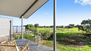 Een houten terras met een overdekt gedeelte en uitzicht op een groen landschap met bomen en een hek.