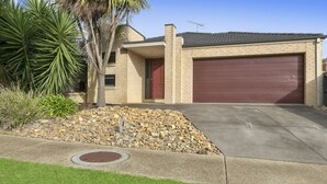 A two-story house with a red garage door, a stone foundation, and a small garden with rocks and plants. - Ocean View Crescent 59 Torquay Pet Friendly (TORQUAY)