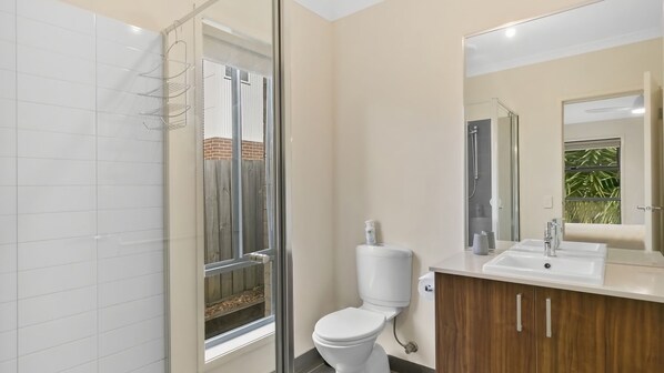 A modern bathroom with a glass shower enclosure, a toilet, a sink, and a large mirror. - Ocean View Crescent 59 Torquay Pet Friendly (TORQUAY)