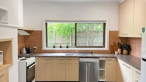 A modern kitchen with wooden cabinets, a built-in oven, a dishwasher, and a window with a view of greenery outside. - Immaculately prepared property is only 40 metres from the foreshore (TORQUAY)