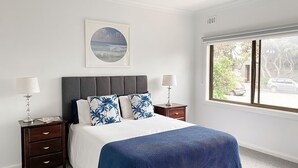 A bedroom with a bed, two bedside tables, a window with a view of the street, and a framed picture on the wall. - Immaculately prepared property is only 40 metres from the foreshore (TORQUAY)