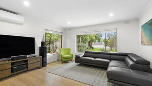 A modern living room with a large flat-screen TV, a grey sectional sofa, a green armchair, and a wooden entertainment unit. - Puebla Casa 17  Walk to Beach & Shops (TORQUAY)