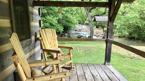 Une chaise berçante en bois sur une véranda, avec vue sur une cascade et la verdure environnante.