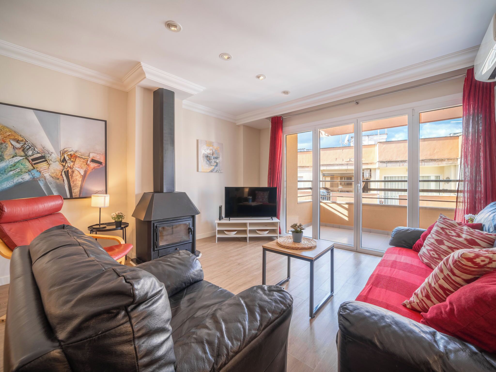 A living room with a fireplace, leather sofas, a TV, and a balcony with a view of buildings.