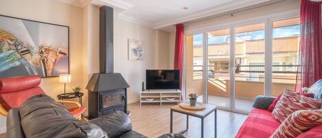 A living room with a fireplace, leather sofas, a TV, and a balcony with a view of buildings.
