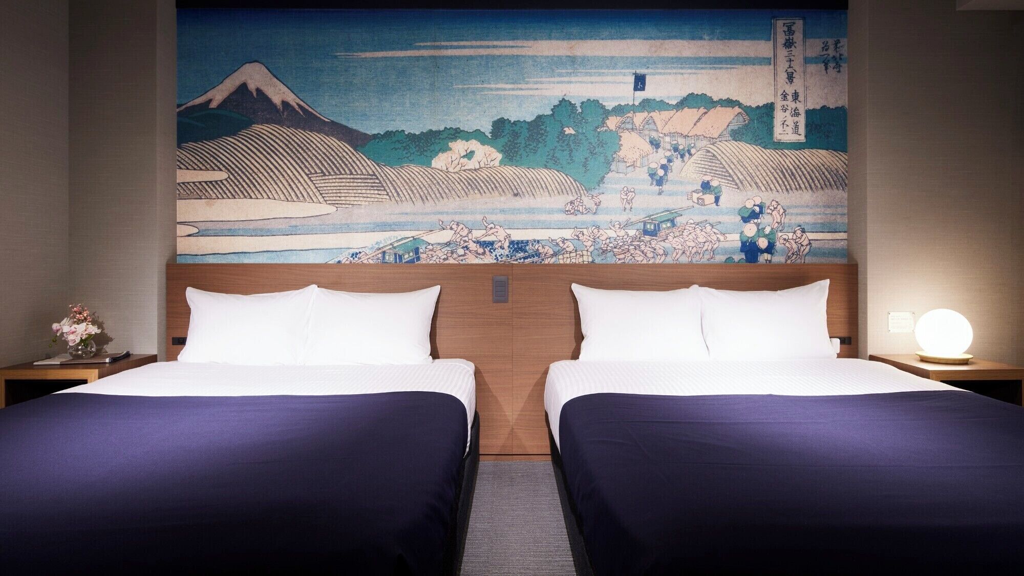 A hotel room with two beds, a traditional Japanese painting on the wall, and a nightstand with a lamp.