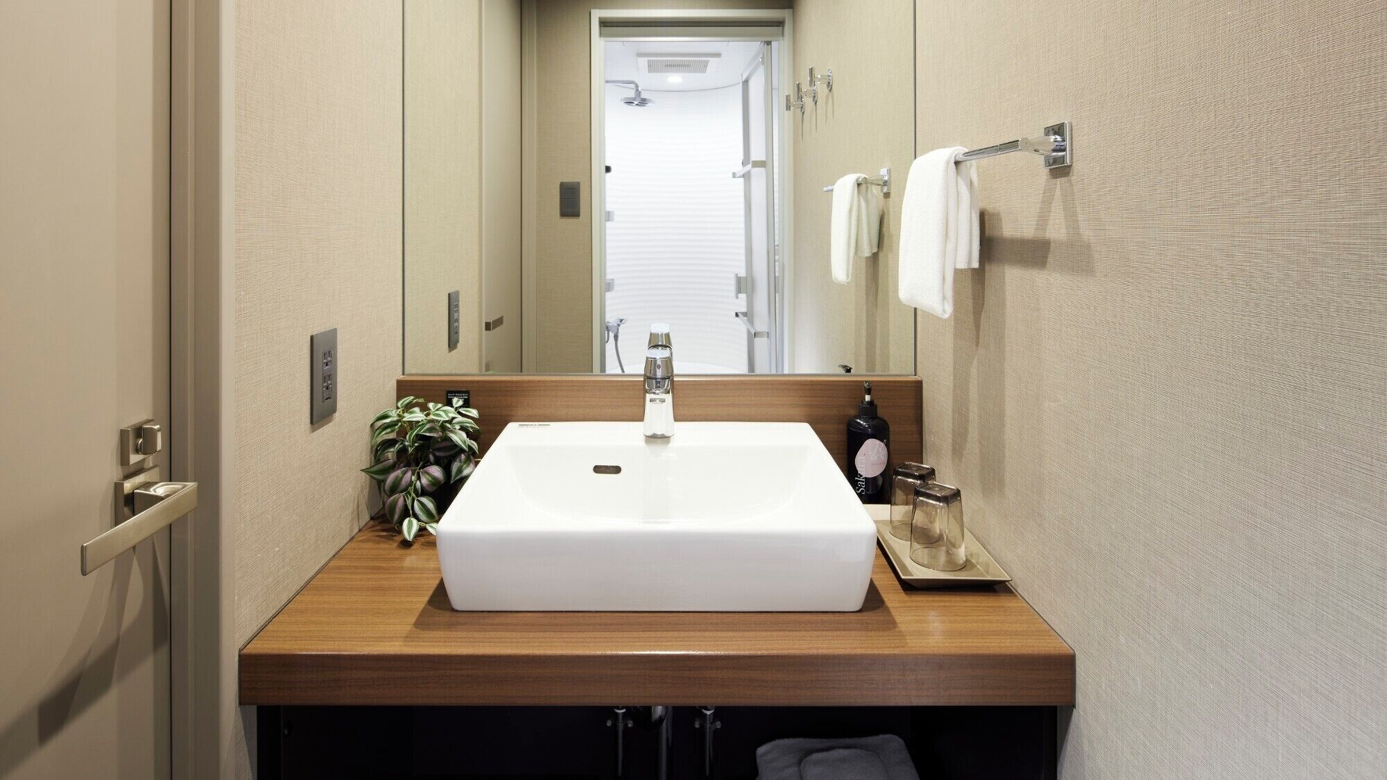 A modern bathroom with a rectangular sink, a mirror, a towel rack, and a potted plant.