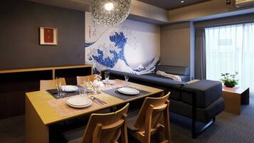 A dining area with a wooden table set for two, a sofa, and a wall with a blue wave design.