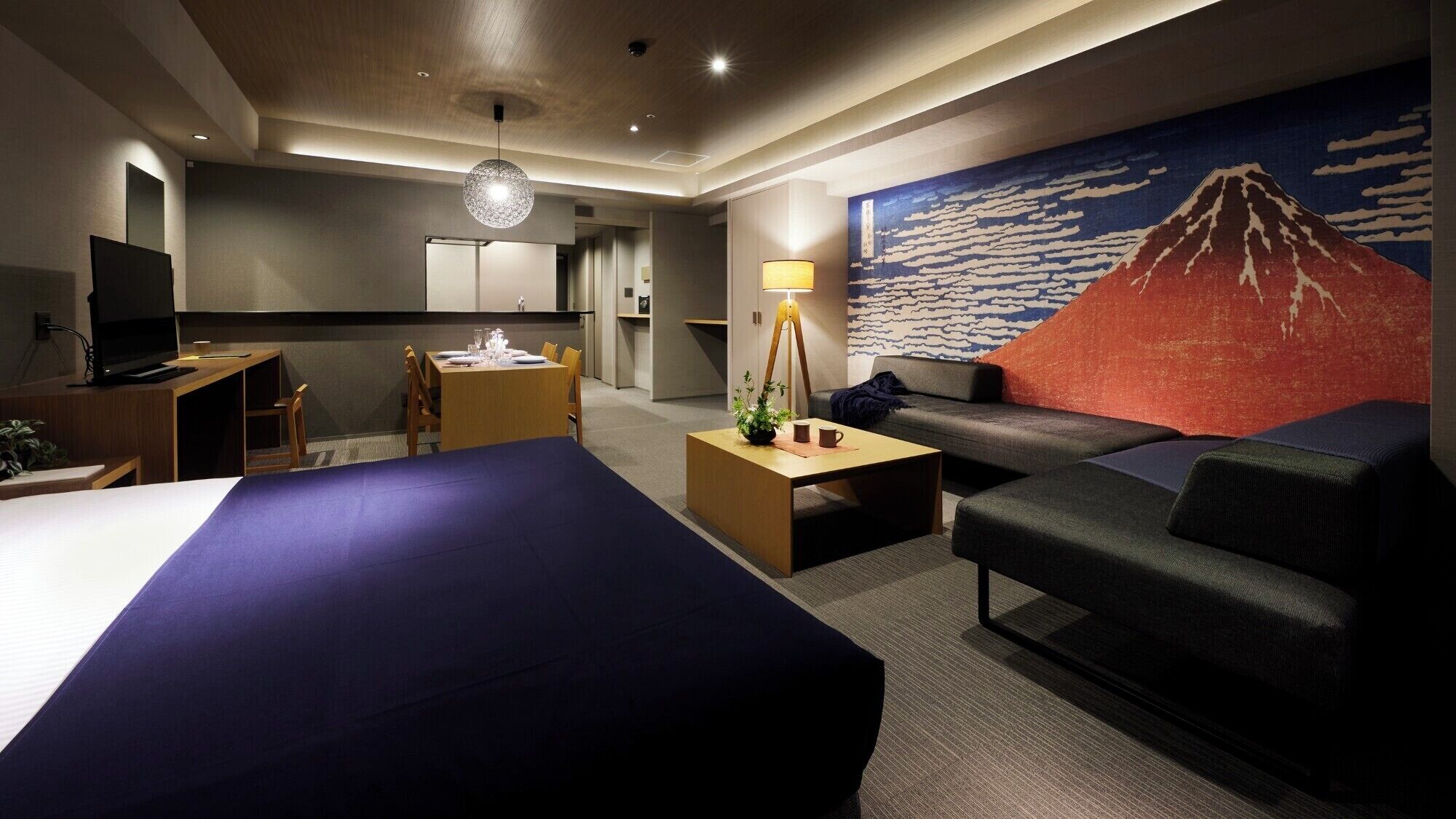 Ein Hotelzimmer mit zwei Betten, einem Schreibtisch, einer Couch, einem Couchtisch und einem Gemälde einer Berglandschaft.