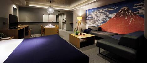 A hotel room with two beds, a desk, a sofa, a coffee table, and a painting of a mountain.