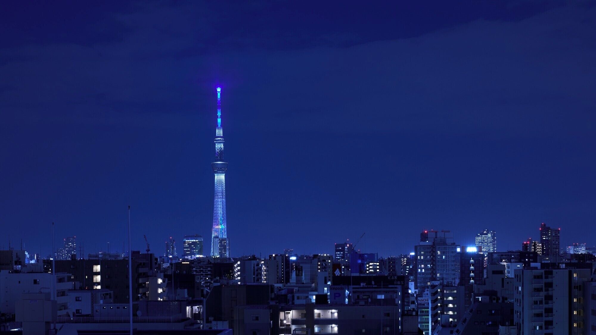 A cityscape with a prominent tower lit up in blue.