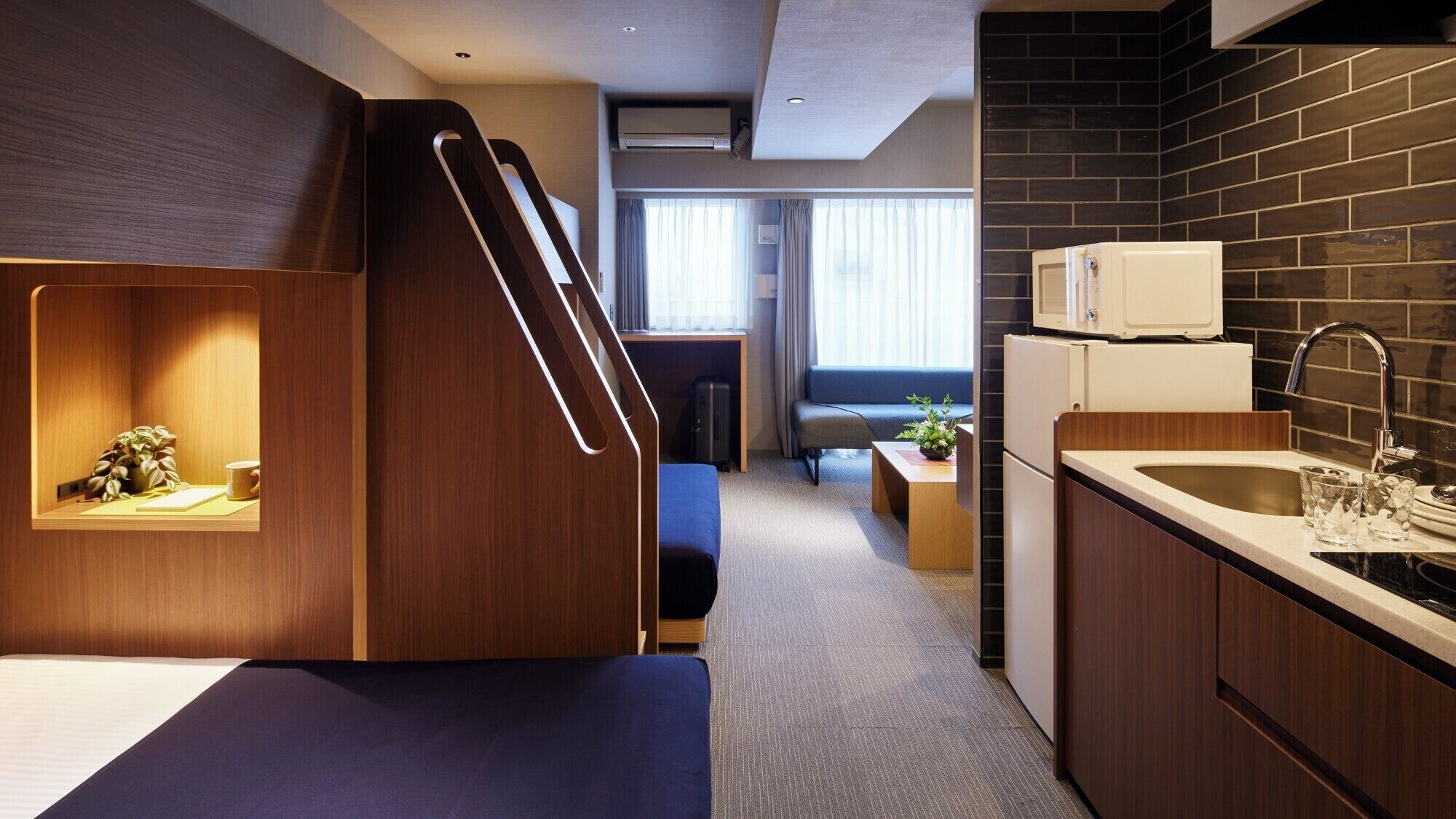 A compact hotel room with a kitchenette, a seating area, and a view of the city.